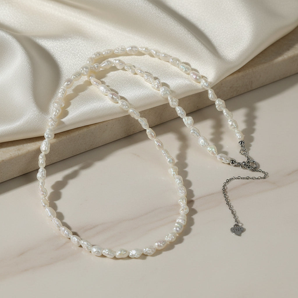 Lyra delicate rice pearl strand on marble, fine white rice pearls with sterling silver clasp and heart charm
