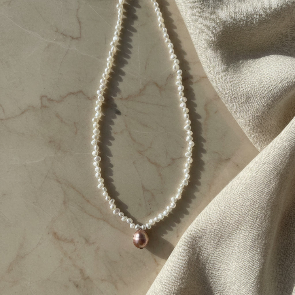 Laevié Vienna necklace on marble, fine white freshwater pearl strand with a mauve pendant pearl and gold-tone fittings