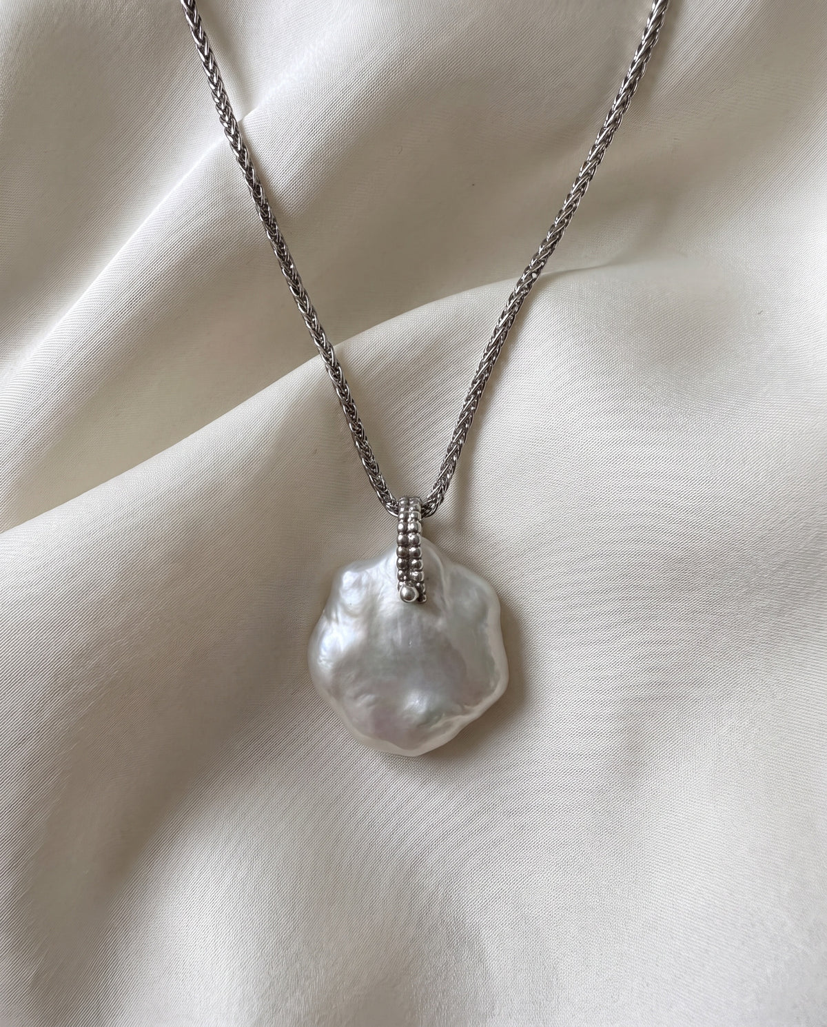 Laevié Flora petal pendant necklace on ivory silk, one flat irregular cultured freshwater pearl on a braided sterling silver chain with a granulated silver bar at the pearl's upper edge