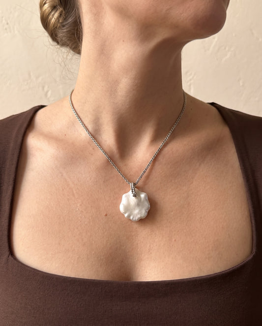 Laevié Flora petal pendant necklace worn, the pearl resting just below the collarbone on a fine braided sterling silver chain